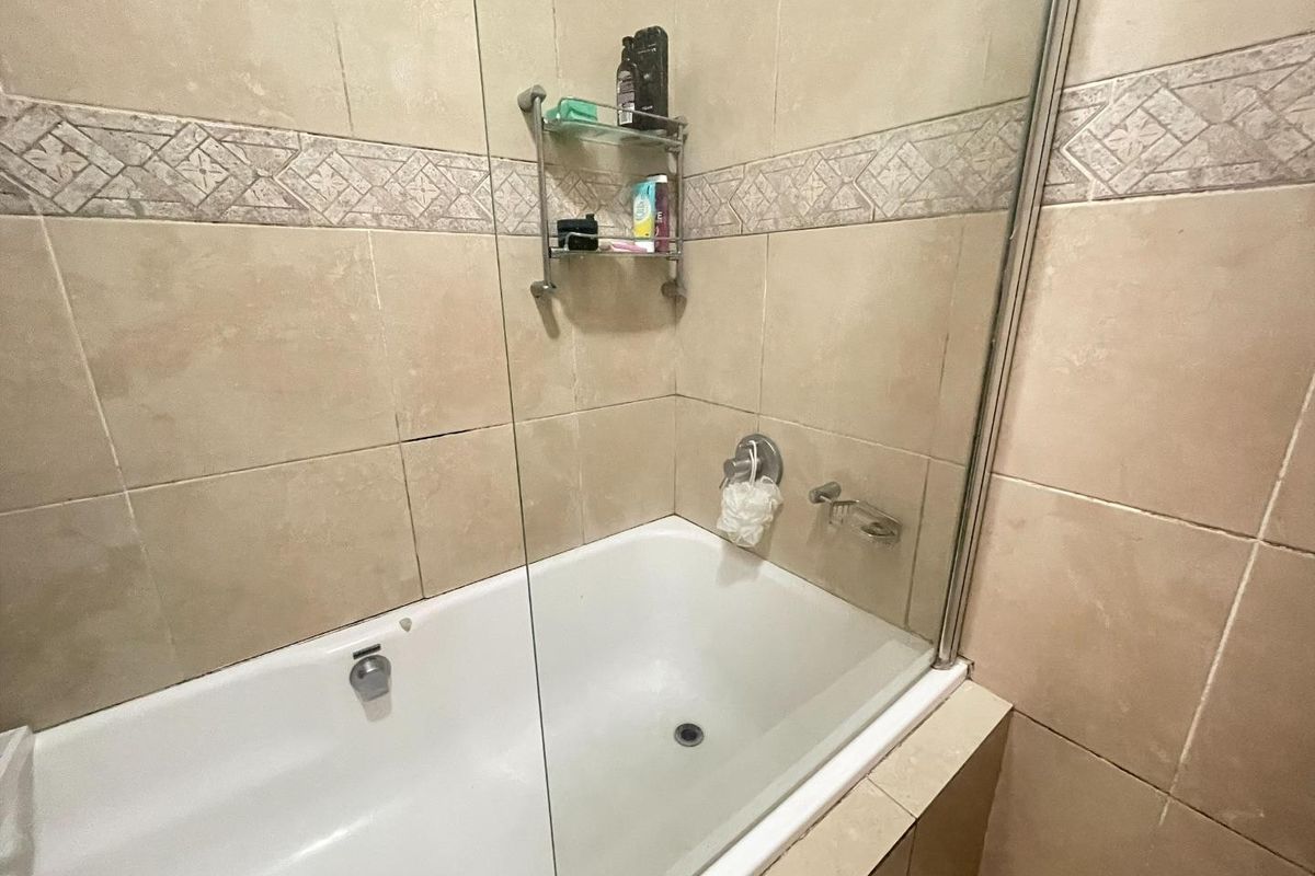 A bathroom featuring a bathtub with a glass shower screen and neutral ceramic wall tiling.