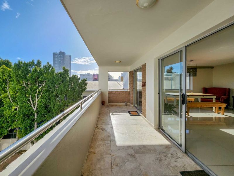 Spacious covered balcony featuring tiled flooring, a modern stainless steel balustrade, and large sliding glass doors providing seamless access to the interior living area.