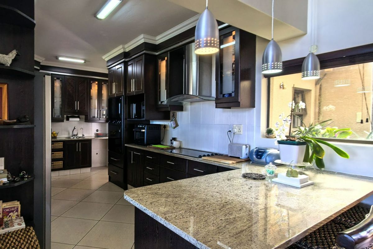 Spacious kitchen featuring dark wood cabinetry, granite countertops, stainless steel appliances, and a breakfast bar with pendant lighting.