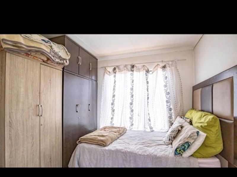 A compact bedroom featuring built-in wooden cupboards and a window with natural light.