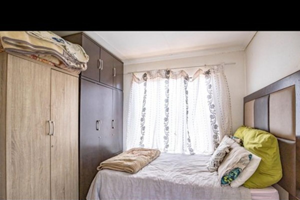 A compact bedroom featuring built-in wooden cupboards and a window with natural light.