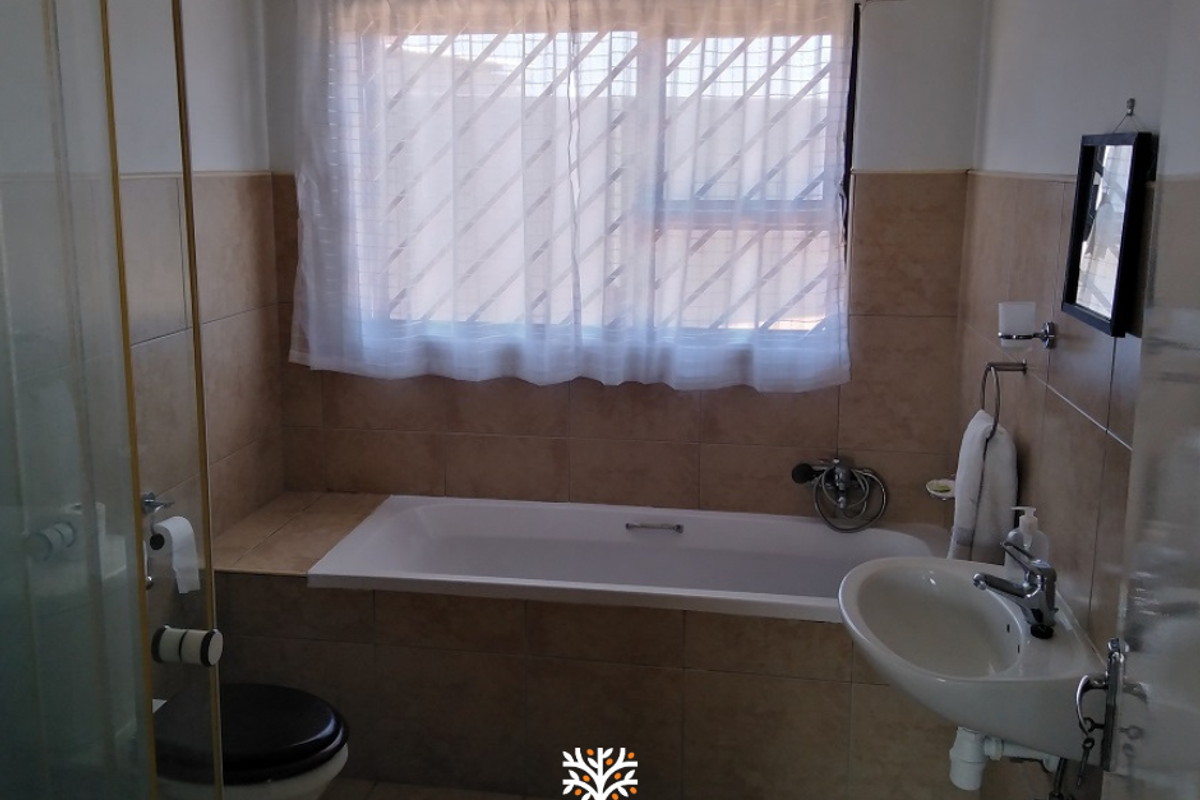 A functional bathroom featuring a built-in bathtub, a separate glass-enclosed shower, a wall-mounted basin, and tiled walls.