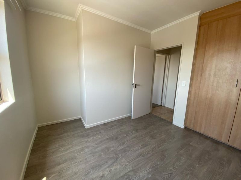 A clean, empty bedroom featuring modern laminate flooring, neutral walls, and built-in wooden cupboards, offering a versatile space ready for personalization.