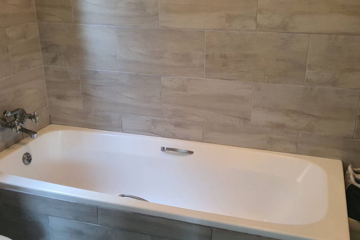 A modern bathroom featuring a built-in bathtub with wood-look tiled surround and wall cladding.