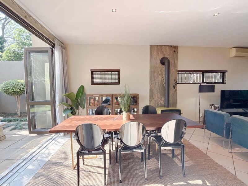 Spacious open-plan living and dining area featuring a striking stone-clad fireplace, tiled flooring, and large glass doors opening to the outdoor patio.