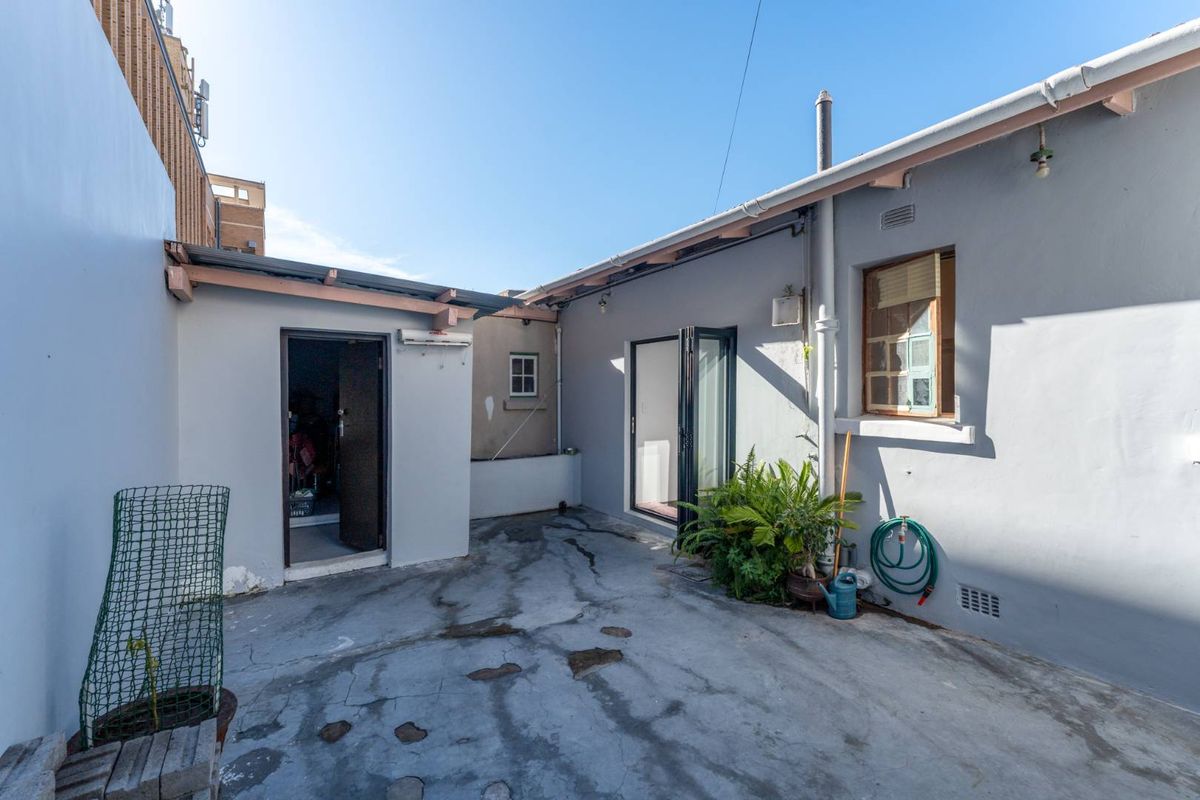 A rear courtyard area featuring a concrete patio, bi-fold doors, and exposed timber roof beams, offering potential for outdoor living space improvement.