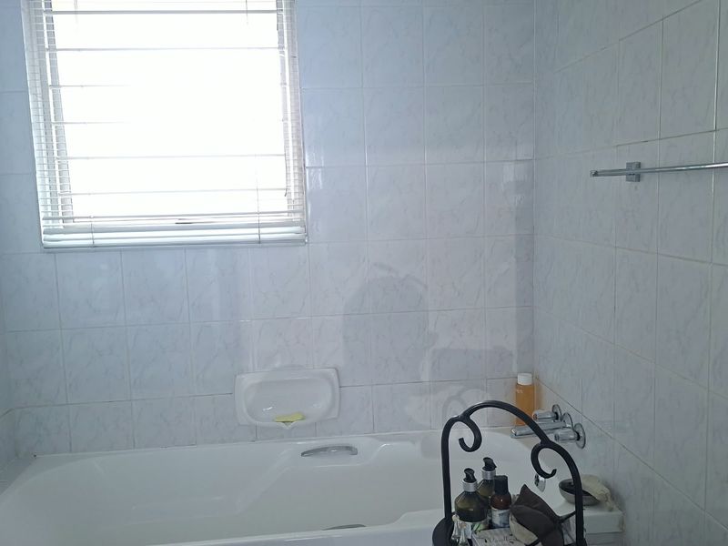 A functional bathroom featuring a built-in bathtub, tiled walls, and a window with a venetian blind.