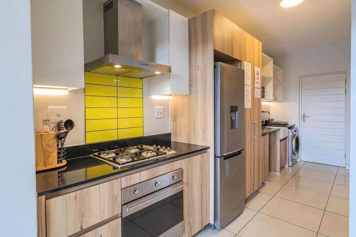 Modern kitchen featuring wood-finish cabinetry, stone countertops, a gas hob, built-in oven, and integrated laundry facilities with tiled flooring throughout.