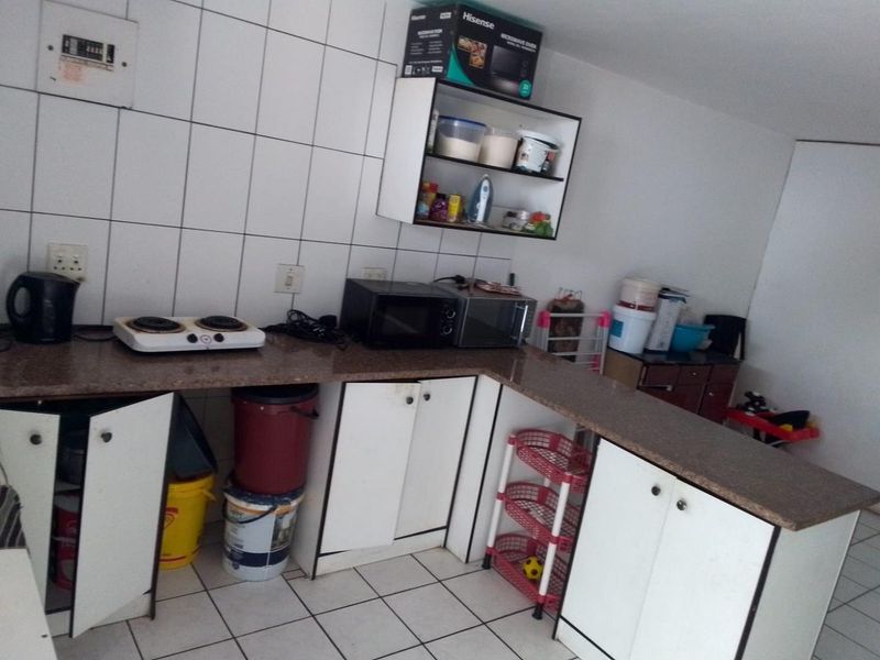 A functional kitchen area featuring granite countertops, tiled splashbacks, and built-in cabinetry, currently showing signs of wear and requiring maintenance.