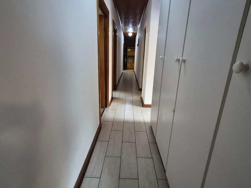 A long hallway featuring tiled flooring, a timber-paneled ceiling, and extensive built-in storage cupboards along one side.