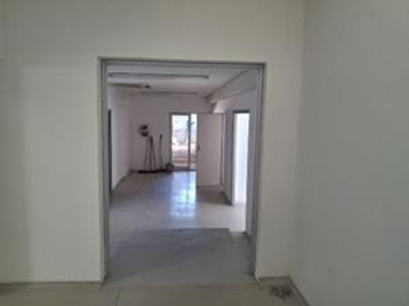 An empty office space featuring tiled flooring and fluorescent lighting, viewed through an open doorway.