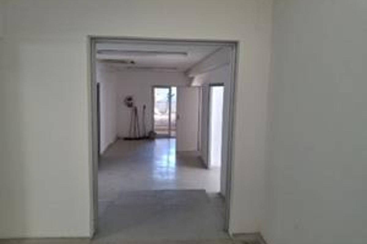 An empty office space featuring tiled flooring and fluorescent lighting, viewed through an open doorway.