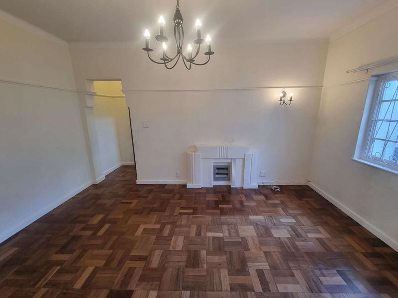 Spacious living room featuring original parquet flooring, a built-in fireplace, decorative coved cornicing, and a classic chandelier, offering a bright and neutral blank canvas.