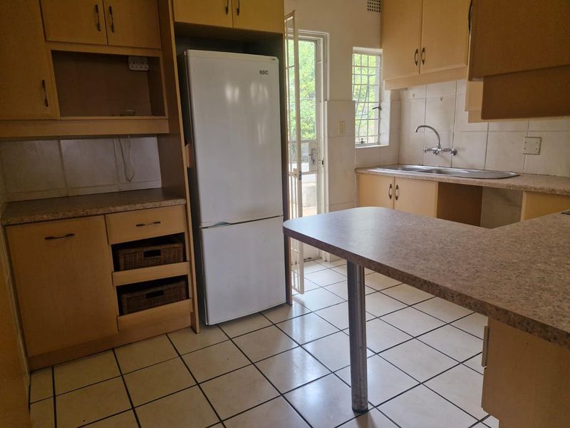 A functional kitchen featuring laminate cabinetry, tiled flooring, and a double basin sink, with direct access to the exterior via a security gate.