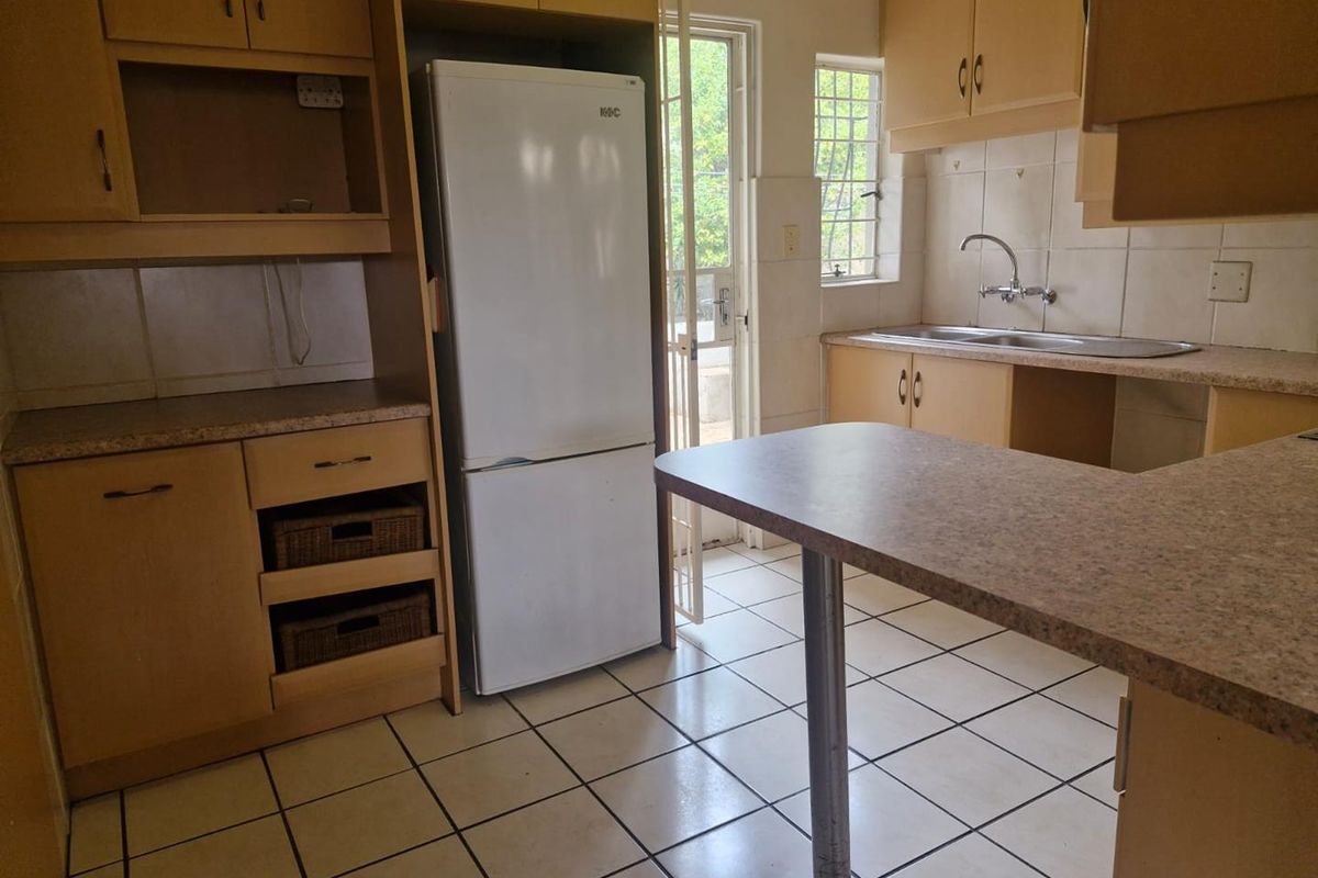 A functional kitchen featuring laminate cabinetry, tiled flooring, and a double basin sink, with direct access to the exterior via a security gate.