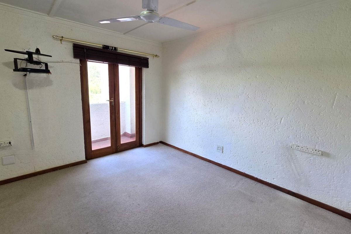 An empty bedroom featuring textured walls, carpet flooring, a ceiling fan, and double glass doors leading to an outdoor area.