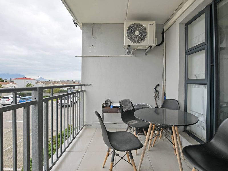 A functional balcony featuring tiled flooring, a metal balustrade, and a wall-mounted air conditioning unit, offering an outdoor space with neighbourhood views.
