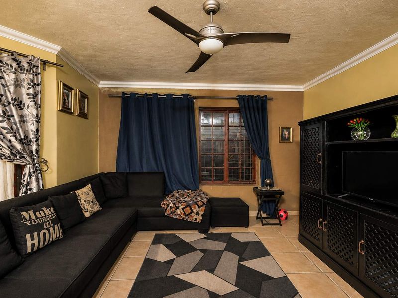 A living room featuring tiled flooring, a ceiling fan, and crown molding, showing signs of wear including ceiling water stains and wall paint damage.