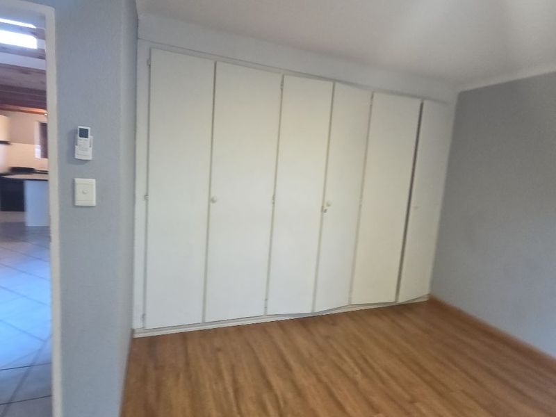 An empty bedroom featuring laminate flooring and a large wall of built-in cupboards with some visible misalignment.