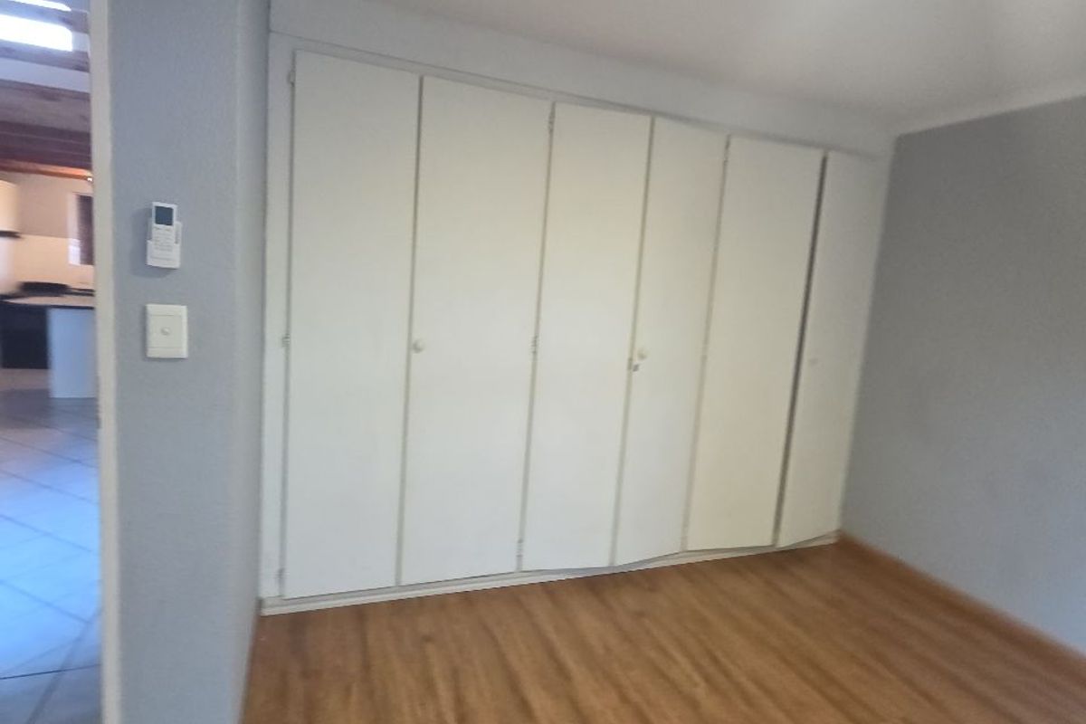 An empty bedroom featuring laminate flooring and a large wall of built-in cupboards with some visible misalignment.