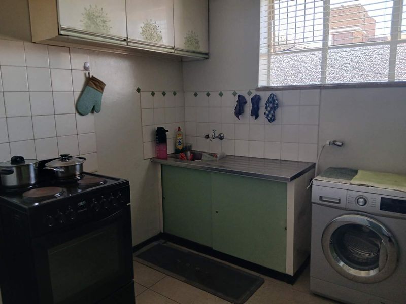 A functional kitchen featuring a stainless steel sink, tiled backsplash, built-in cabinetry, and space for a freestanding stove and washing machine.