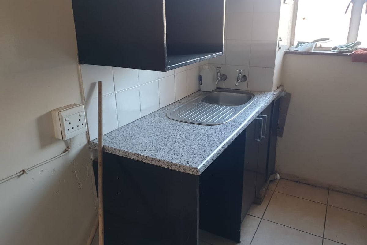 A compact kitchen area featuring a single sink, laminate countertop, and dark cabinetry with tiled splashbacks.