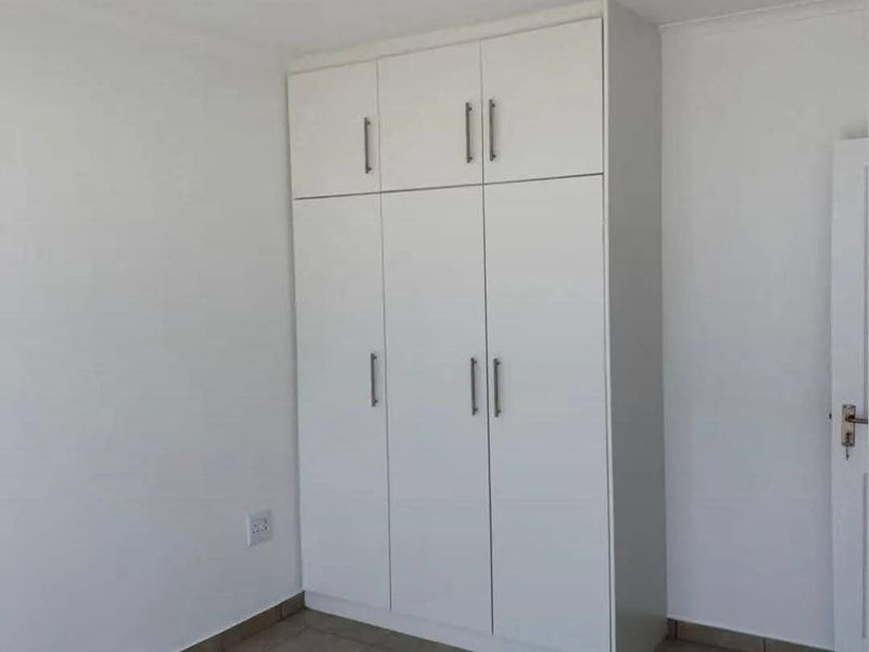 A clean, empty bedroom featuring neutral tiled flooring and a white built-in wardrobe with overhead storage compartments.