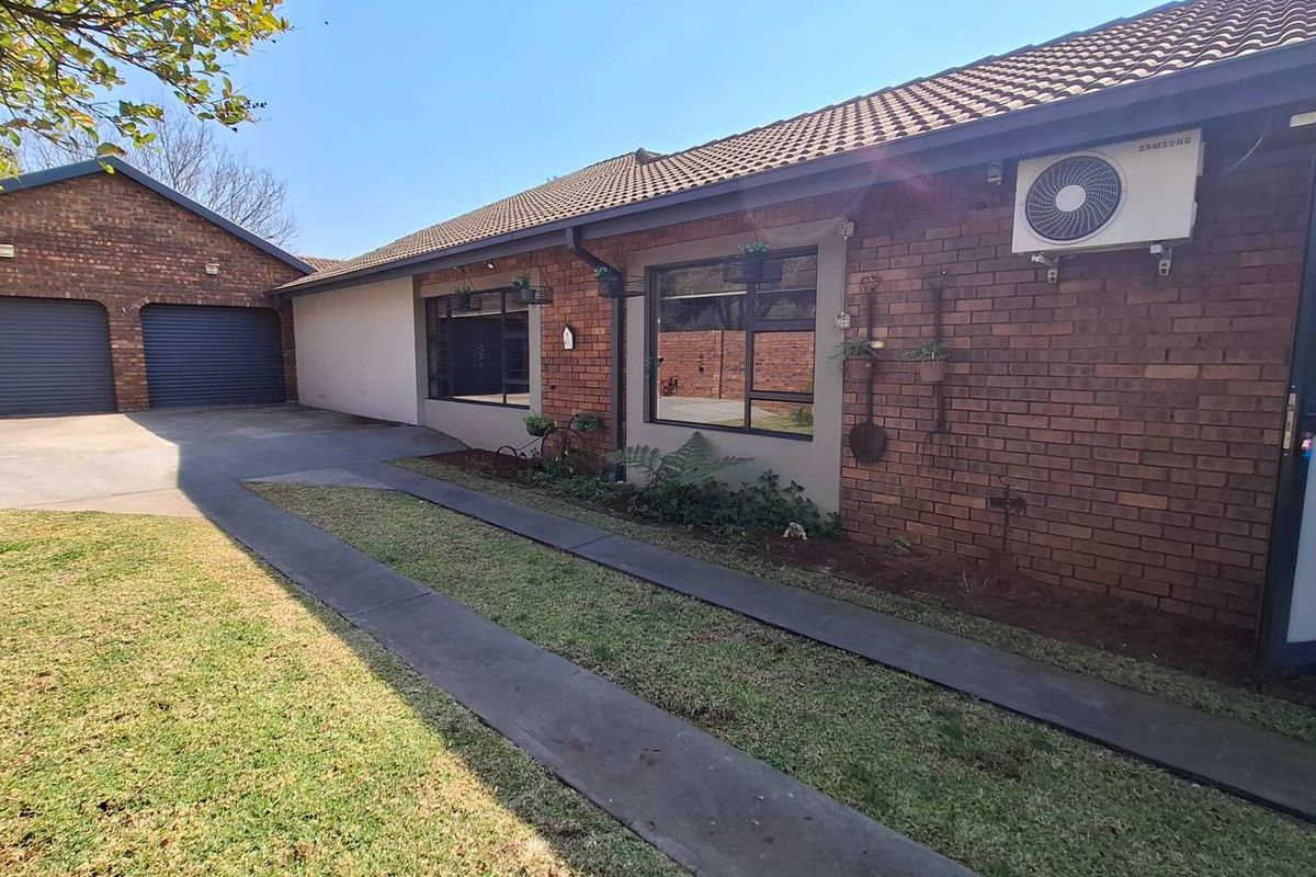 Rear view of the property featuring a brick facade, tiled roof, double garage, and a paved driveway leading to the garden area.