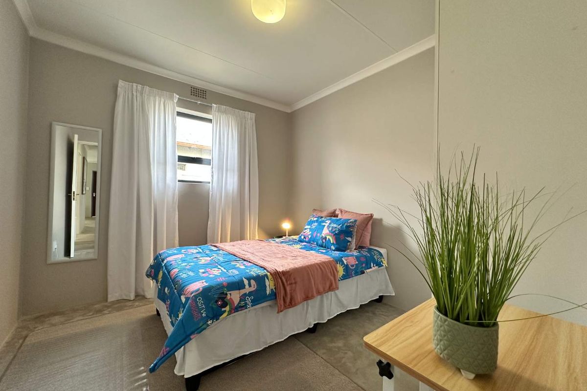 A well-maintained bedroom featuring neutral wall tones, carpeted flooring, a built-in wardrobe, and a ceiling light fixture.