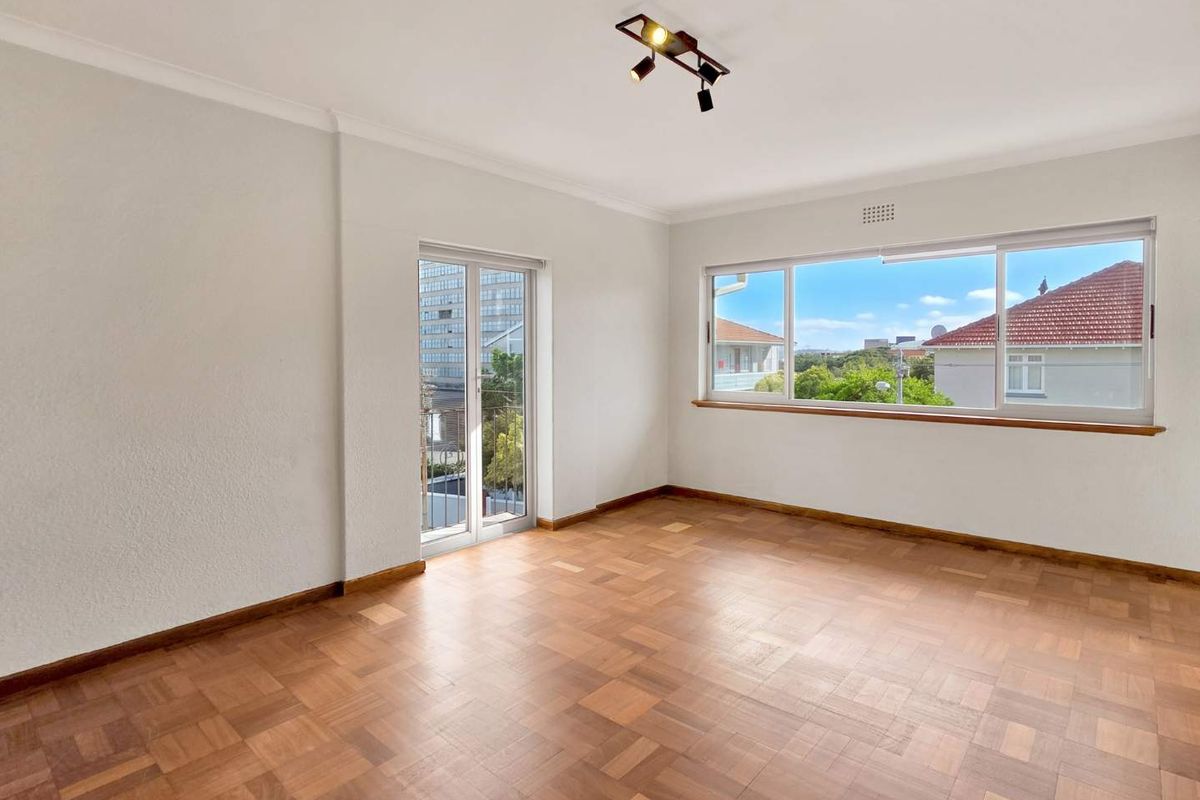 A bright and spacious living area featuring polished parquet flooring, large windows, and a glass door leading to an outdoor space.