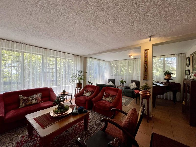 Spacious open-plan living area featuring large windows with natural light, tiled flooring, and a textured ceiling.