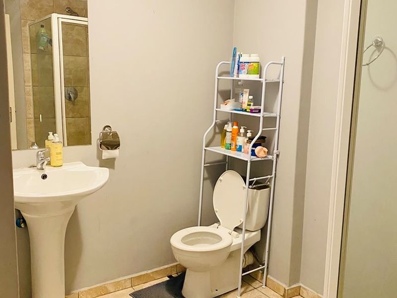 A functional bathroom featuring a pedestal basin, toilet, and a separate shower enclosure with tiled flooring and neutral wall finishes.