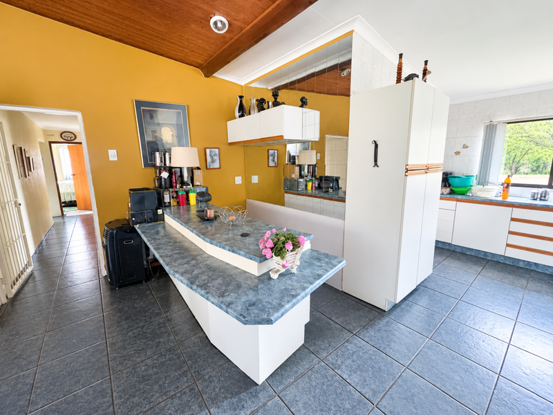 A dated kitchen featuring tiled flooring, timber ceiling, laminate countertops, and a mirrored splashback, offering potential for a modern renovation.