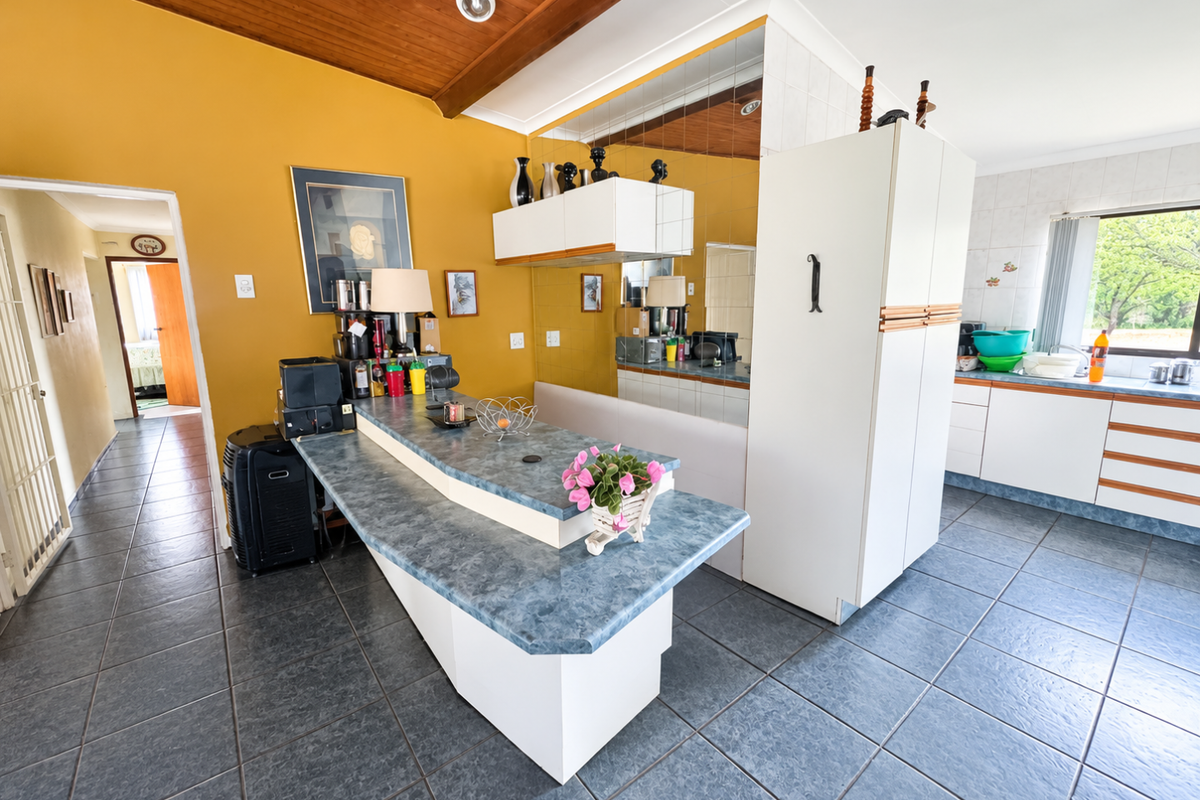 A dated kitchen featuring tiled flooring, timber ceiling, laminate countertops, and a mirrored splashback, offering potential for a modern renovation.