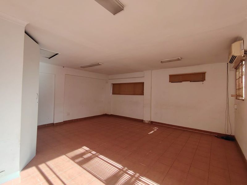 An empty, functional office space featuring tiled flooring, built-in storage, air conditioning, and natural light through venetian blinds.