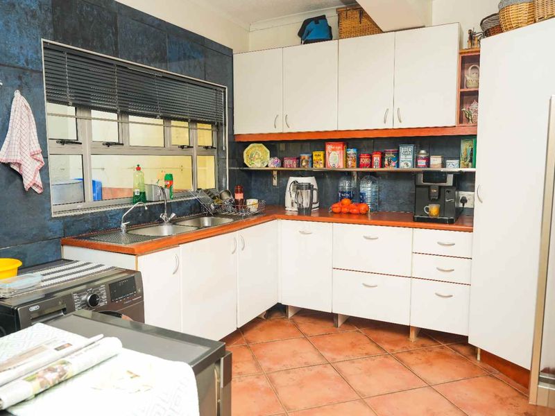 A functional kitchen featuring white cabinetry, laminate countertops, a double stainless steel sink, and dark tiled splashbacks with terracotta floor tiles.