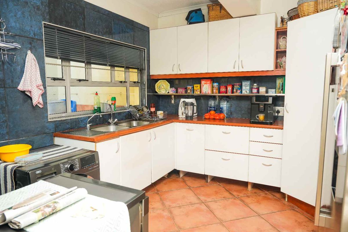 A functional kitchen featuring white cabinetry, laminate countertops, a double stainless steel sink, and dark tiled splashbacks with terracotta floor tiles.