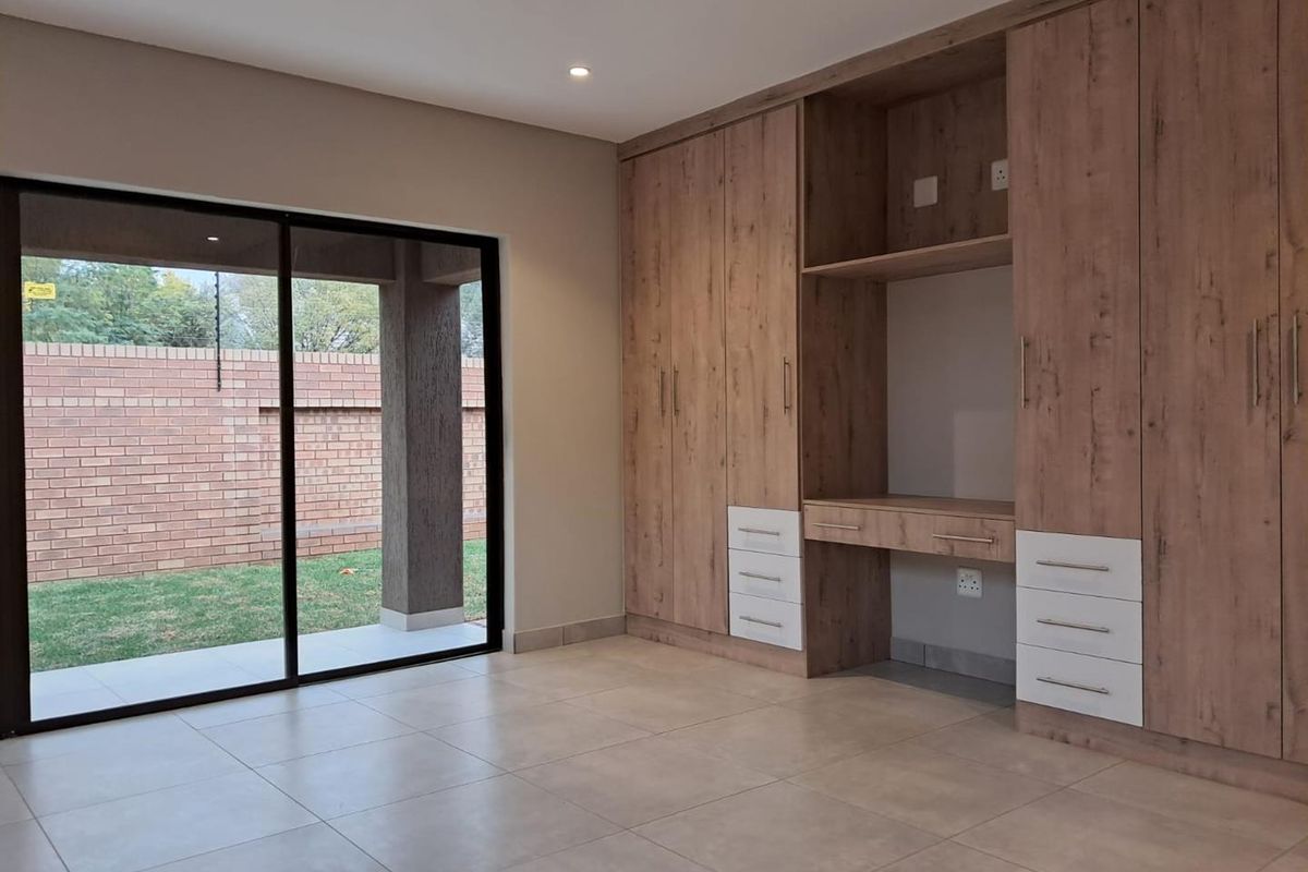 A bright bedroom featuring modern built-in wooden cabinetry with integrated desk space and large sliding glass doors opening to a private patio.
