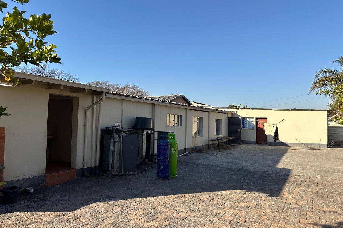 Rear exterior view of the property featuring a paved courtyard area, external access doors, and functional utility space.