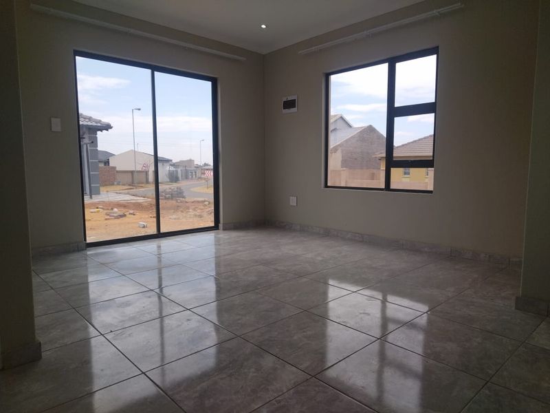 A bright, empty living room featuring polished floor tiles, modern aluminium window frames, and a sliding glass door leading to the exterior.