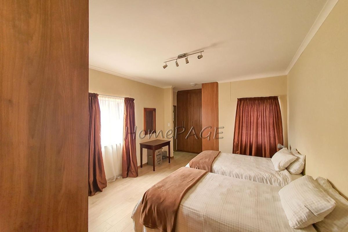 A spacious bedroom featuring built-in wooden cupboards, neutral wall finishes, and track lighting.
