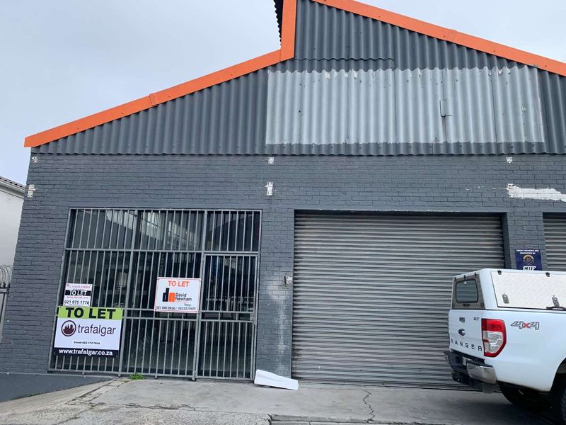 Front elevation of a retail or industrial unit featuring a roller shutter door, security gate, and brick facade with signage.