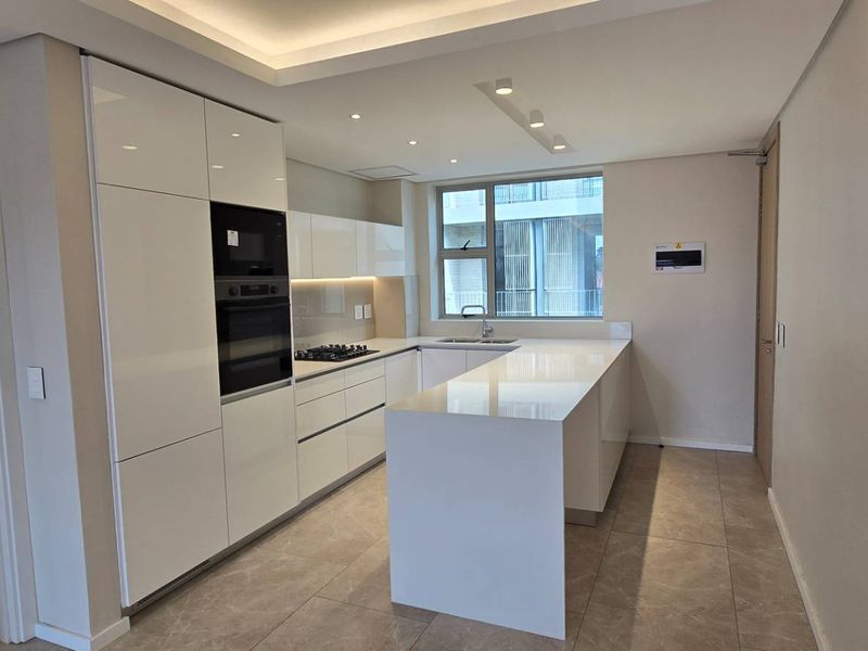 Modern kitchen featuring sleek white cabinetry, stone countertops, integrated appliances, and recessed lighting, offering a clean and functional culinary space.