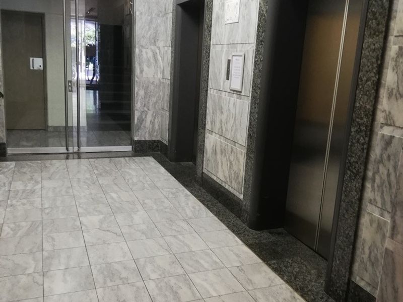 Professional office building lobby featuring marble wall cladding, tiled flooring, and a dual elevator bank with glass entrance doors.