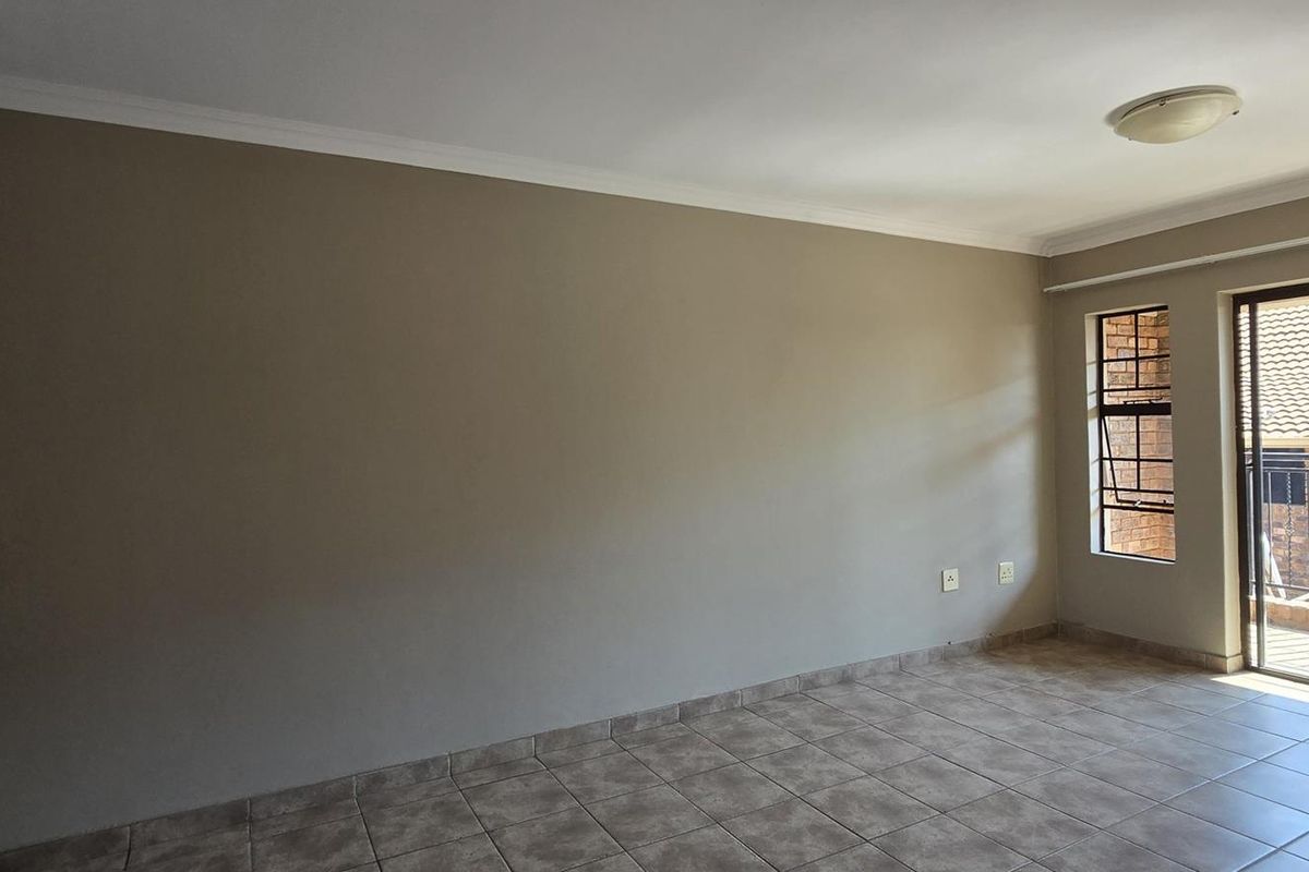 An empty living room featuring neutral walls, tiled flooring, and a sliding glass door providing access to an outdoor balcony area.