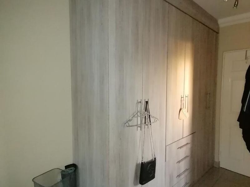 A bedroom featuring floor-to-ceiling built-in cupboards with a light wood-grain finish and integrated drawer storage.