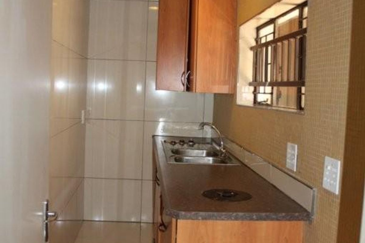 A compact galley-style kitchen featuring built-in wooden cabinetry, a stainless steel sink, and tiled wall finishes.