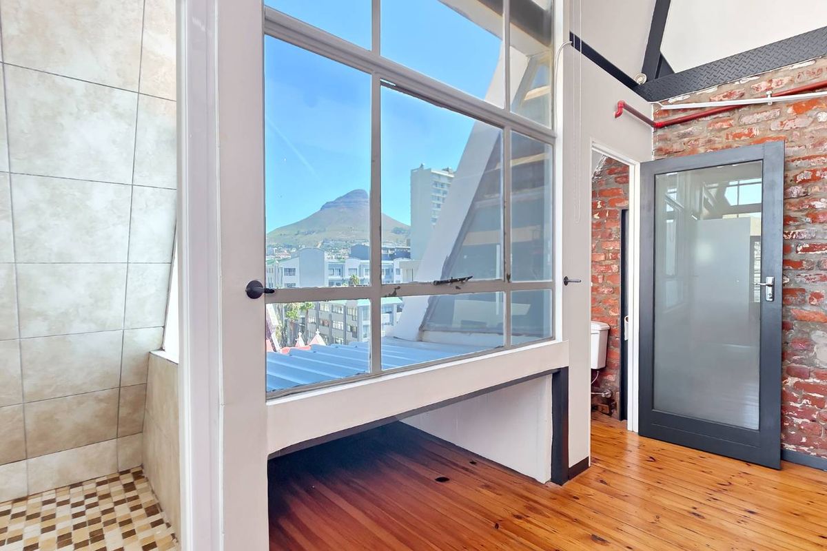 An industrial-style bedroom featuring exposed brick walls, timber flooring, and a large window offering scenic mountain views.