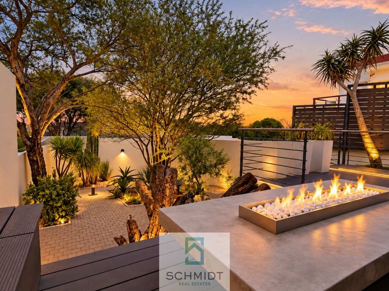 A beautifully landscaped outdoor patio featuring composite decking, a modern built-in gas fireplace, and ambient wall lighting, perfect for evening entertaining.