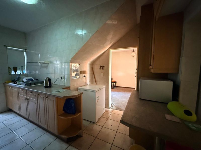 A dated kitchen featuring laminate cabinetry, tiled splashbacks, and ceramic flooring, with an adjacent room visible through the doorway.